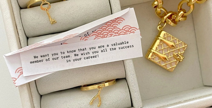 Fortune that reads “We want you to know that you are a valuable member of our team. We wish you all the success in your career!” next to a Secret Diary Book Locket and Wishbone Charm Ring and Key Charm Ring.